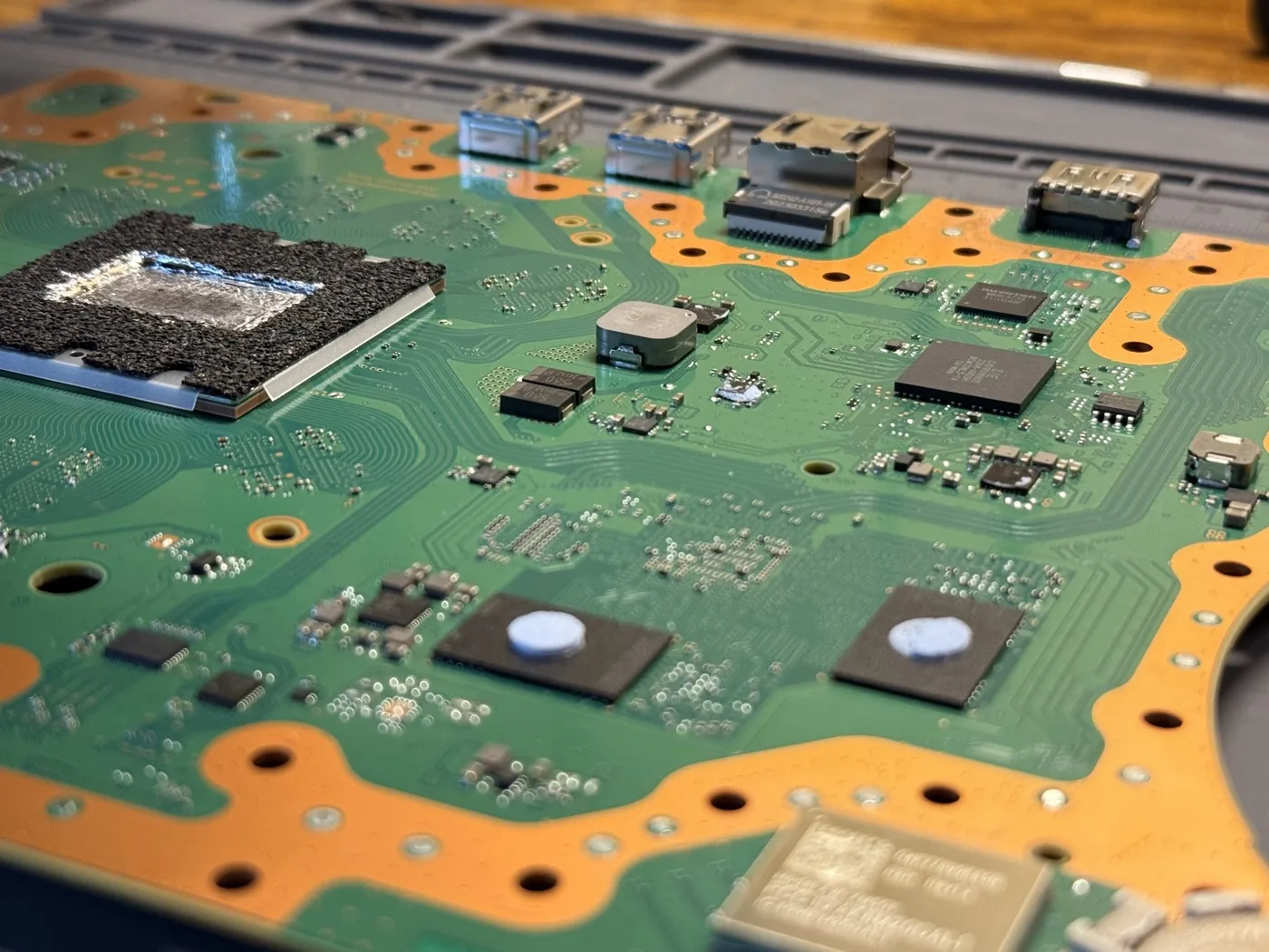 A PS5 mainboard fully exposed on the repair bench, showing the HDMI and USB ports, APU, and thermal pad